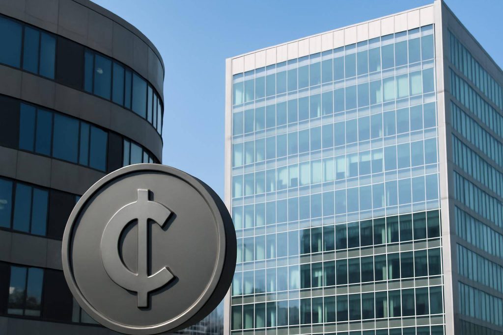 A circular sign with a cent symbol stands in front of two modern office buildings with glass and concrete exteriors under a clear blue sky.