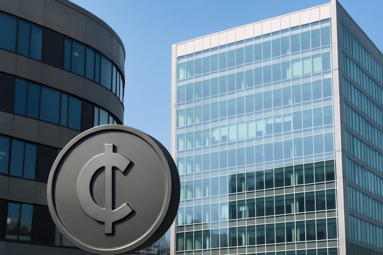 A circular sign with a cent symbol stands in front of two modern office buildings with glass and concrete exteriors under a clear blue sky.